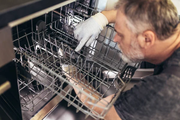 Portrait Of Male Technician Repairing Dishwasher In Kitchen