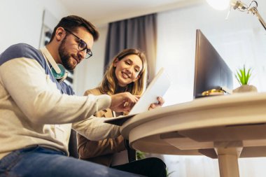 Genç çift evde bilgisayar ve dijital tablet üzerinde birlikte iş yapıyor..