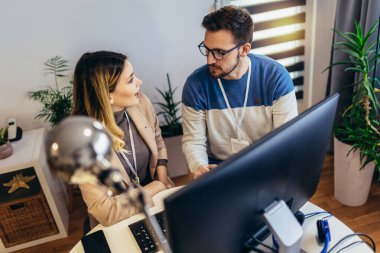 Başarılı genç çift, evde masada otururken bilgisayar başında birlikte çalışıyorlar.