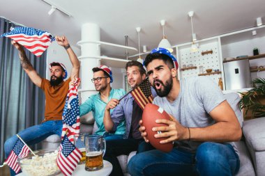 Arkadaşlar birlikte spor ligine tezahürat yapıyor, şampiyonluğu izlerken rugby topu tutuyorlar..