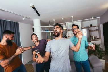 Yakışıklı genç adam mikrofonla şarkı söylüyor, modern dairede arkadaşlarıyla karaoke yapıyor.