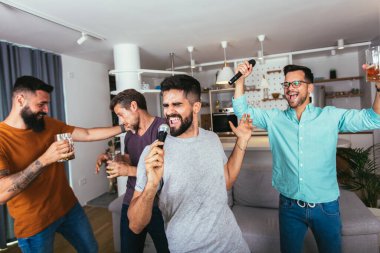 Yakışıklı genç adam mikrofonla şarkı söylüyor, modern dairede arkadaşlarıyla karaoke yapıyor.
