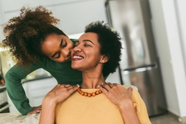 Evde anneler gününü kutlayan bir kadın ve kız. Kanepede oturan kız. Annesi için yapılmış bir kolye..