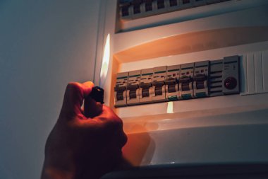 Enerji krizi. Elektrik kesintisi sırasında bir sigorta kutusunu incelemek için elinde çakmak tutuyordu. Karartma konsepti.