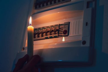 Enerji krizi. Elektrik kesintisi sırasında bir sigorta kutusunu incelemek için elinde mumla karanlıkta el ele tutuşmak. Karartma konsepti.