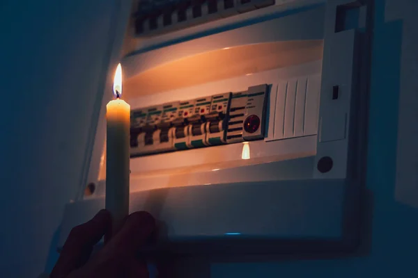 Enerji krizi. Elektrik kesintisi sırasında bir sigorta kutusunu incelemek için elinde mumla karanlıkta el ele tutuşmak. Karartma konsepti.
