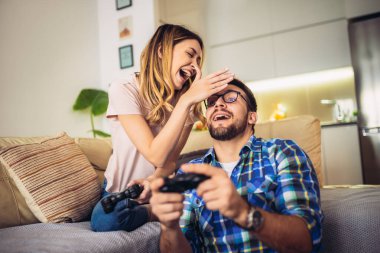 Oturma odasında kanepede oturan ve video oyunu oynayan genç bir çift.