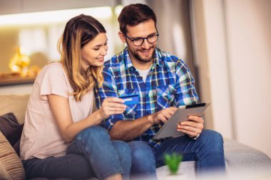 Genç ve neşeli bir çift internetten alışveriş yapıyor. Kredi kartı ve dijital tabletle online çift alışverişi.