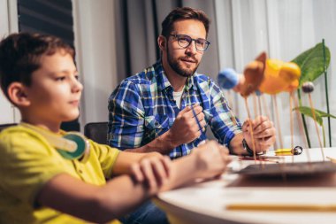 Mutlu okul çocuğu ve babası okuldaki bir bilim projesi için güneş sistemi yapıyorlar.