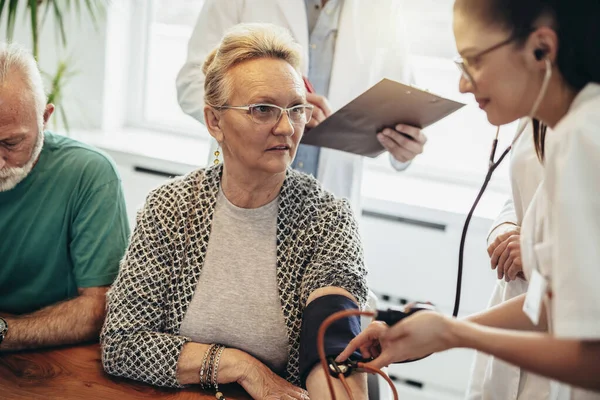 Skupina Mladých Lékařů Při Domácí Návštěvě Seniorů Kontrola Krevního Tlaku — Stock fotografie