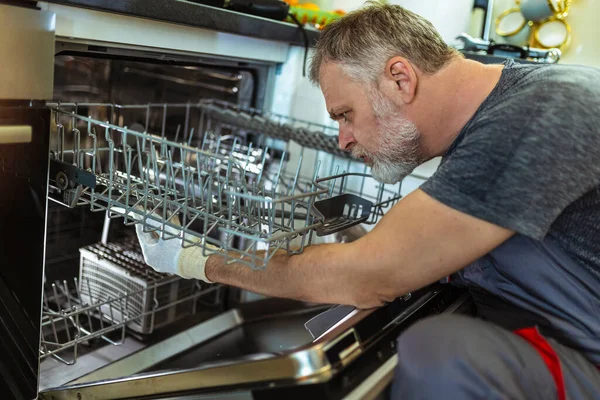 Portrait Of Male Technician Repairing Dishwasher In Kitchen