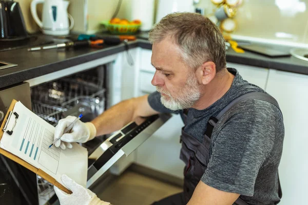 Técnico Masculino Sentado Cerca Del Lavavajillas Escribiendo Portapapeles Cocina Cerca —  Fotos de Stock