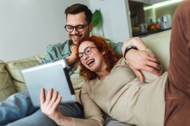 Genç bir çift, oturma odasındaki kanepede oturup internetten medya içeriğini izliyor..
