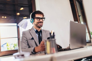 Genç işadamı bilgisayarı kullanıyor ve ofiste video görüşmesi yapıyor.