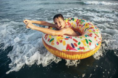 Neşeli çocuk kırılma dalgasında şişirilebilir halka sürüşünde. Seyahat yaşam tarzı, yüzme aktiviteleri. Seçici odak