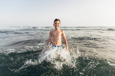 Denizde oynayan mutlu çocuk. Çocuk dışarıda eğleniyor. Yaz tatili ve sağlıklı yaşam tarzı konsepti. Seçici odak