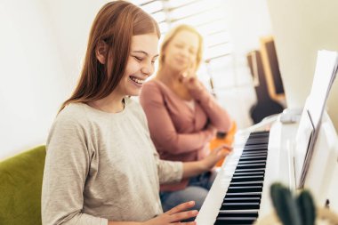 Müzik öğretmeni nasıl piyano çalınacağını gösterir. Kız öğretmenle piyano çalmayı öğreniyor.