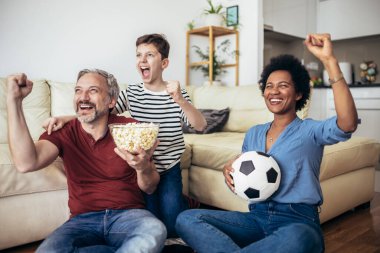 Heyecanlı aile futbolu hayranları birlikte maç izleyip golü kutluyorlar.
