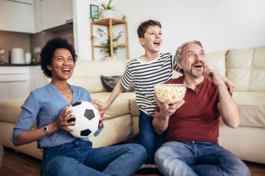 Heyecanlı aile futbolu hayranları birlikte maç izleyip golü kutluyorlar.