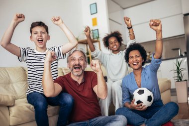 Heyecanlı aile futbolu hayranları birlikte maç izleyip golü kutluyorlar.