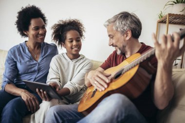 Adam, kızı ve karısı için gitar çalıp şarkı söylüyor..