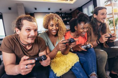 Group of friends playing video games. Happy fellows having fun at home with joysticks playing video games, gesturing and screaming, enjoying time together.
