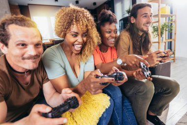 Group of friends playing video games. Happy fellows having fun at home with joysticks playing video games, gesturing and screaming, enjoying time together.