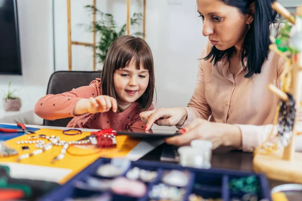 Anne ve küçük anaokulu kızları evde birlikte bilezik yaparken eğleniyorlar.