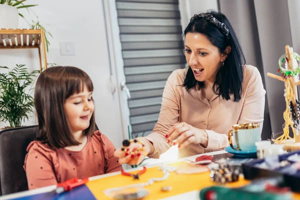 Anne ve küçük anaokulu kızları evde birlikte bilezik yaparken eğleniyorlar.
