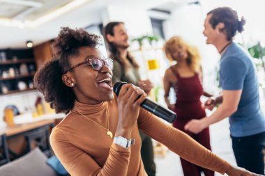 Bir grup genç çok kültürlü arkadaş evde mikrofon kullanarak parti şarkısı söylüyorlar..