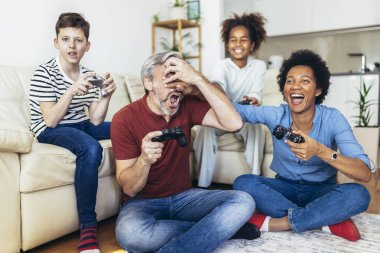 Gülümseyen aile evde birlikte vakit geçiriyorlar. Oturma odasında kanepede oturup video oyunları oynuyorlar..