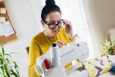 Evinde dikiş makinesine dikiş diken bir kadın. Dikiş makinesinde kadın terzilik işi