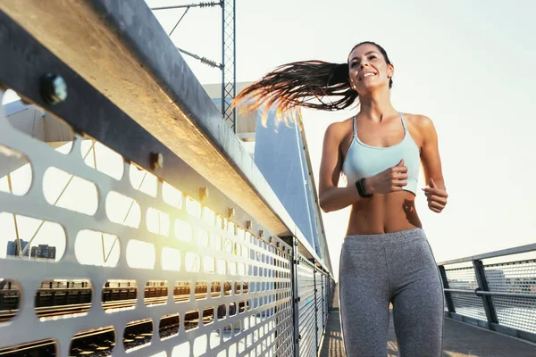 橋の上で街をジョギングする女性ランナー — ストック写真