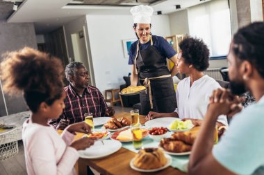 Yemek masasında yemek yiyen çok nesilli Afro-Amerikan bir aile. Beyaz kadın aşçı servis ediyor..