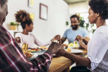 Yemek masasında şükran duası edip el ele tutuşan çok nesilli Afro-Amerikan bir aile.