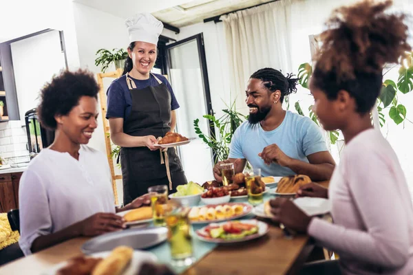 Yemek masasında yemek yiyen çok nesilli Afro-Amerikan bir aile. Beyaz kadın aşçı servis ediyor..