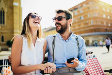 Telefonla alışveriş yaptıktan sonra bankta oturan güzel, gülümseyen genç bir çiftin portresi..