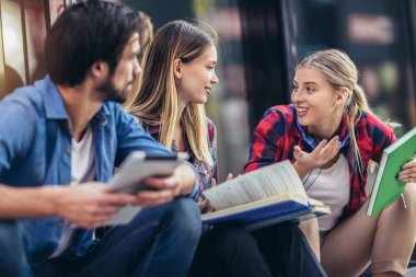 Bir grup mutlu üniversite öğrencisi kampüste otururken konuşuyor..