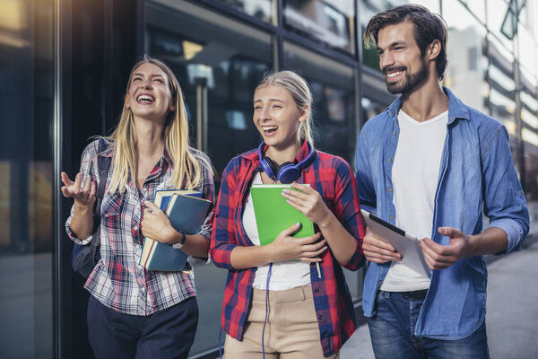 Happy university students walking after the lecture at campus.