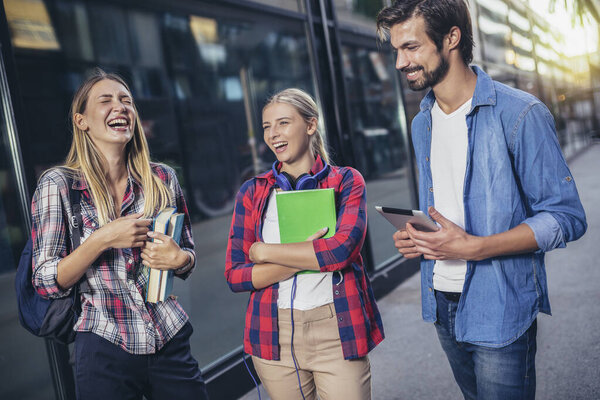 Happy university students walking after the lecture at campus.