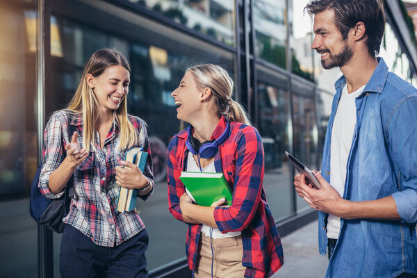 Happy university students walking after the lecture at campus.