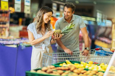 Beautiful young smiling couple choosing fruits in supermarket together