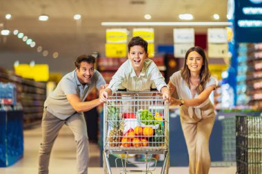 Çocuklu ve alışveriş arabalı mutlu bir aile marketten ya da marketten yiyecek alıyor.