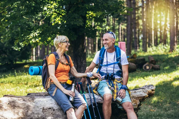Mature couple sitting and resting in the forest after hiking.