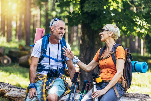 Mature couple sitting and resting in the forest after hiking.