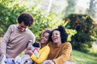 Beautiful young family lying on a picnic blanket with their dog, enjoying an autumn day in park