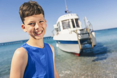 Portrait of a smiling boy on the beach with a tourist boat in the background
