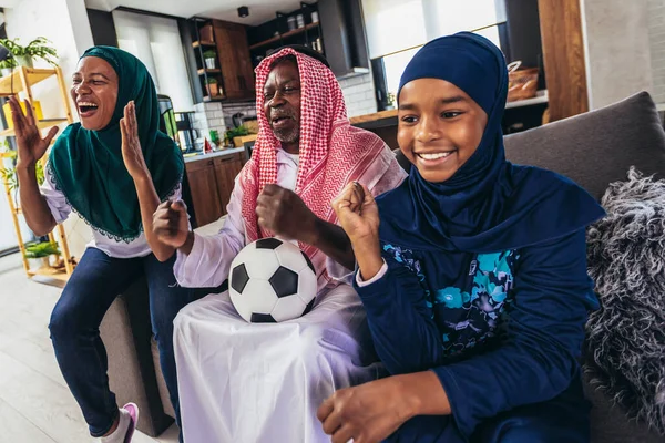 Arab man looking TV at home during a sport event with his family. Watching football game.