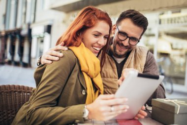 Happy young couple using a digital tablet together at a coffee shop. Young man and woman looking at touch screen computer and smiling.