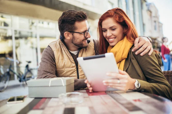 Happy young couple using a digital tablet together at a coffee shop. Young man and woman looking at touch screen computer and smiling.